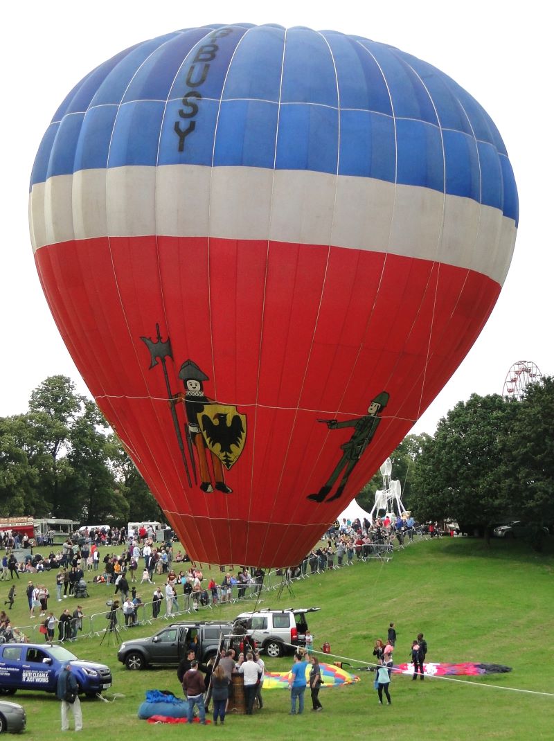 Colour picture of inflated balloon with crew standing around the basket. The balloon has pictures of toy figures on the red lower half with a white band above and a blue top.